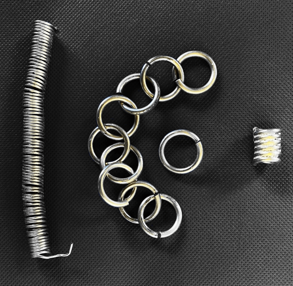 A sterling silver spring, individual rings, and a block of material laid out on a black, fabric mat shown from above.