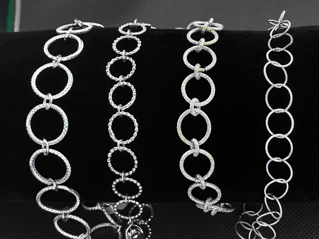 4 silver bracelets made of links of textured wire on a black velvet display stand.